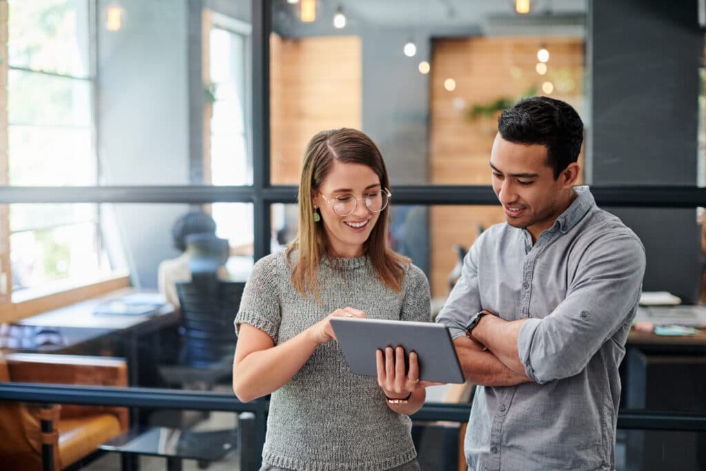 Two business people are looking at a tablet in an office.