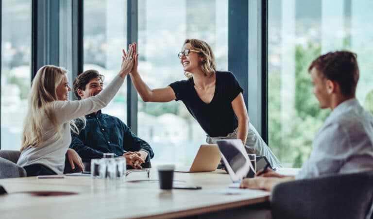 Lächelnde Büroangestellte lernen in einer Peer-to-Peer-Schulung im Büro und geben sich ein High Five.