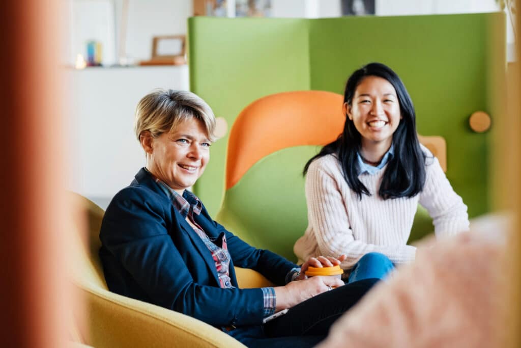 Zwei lächelnde Geschäftsfrauen unterhalten sich im Büro.