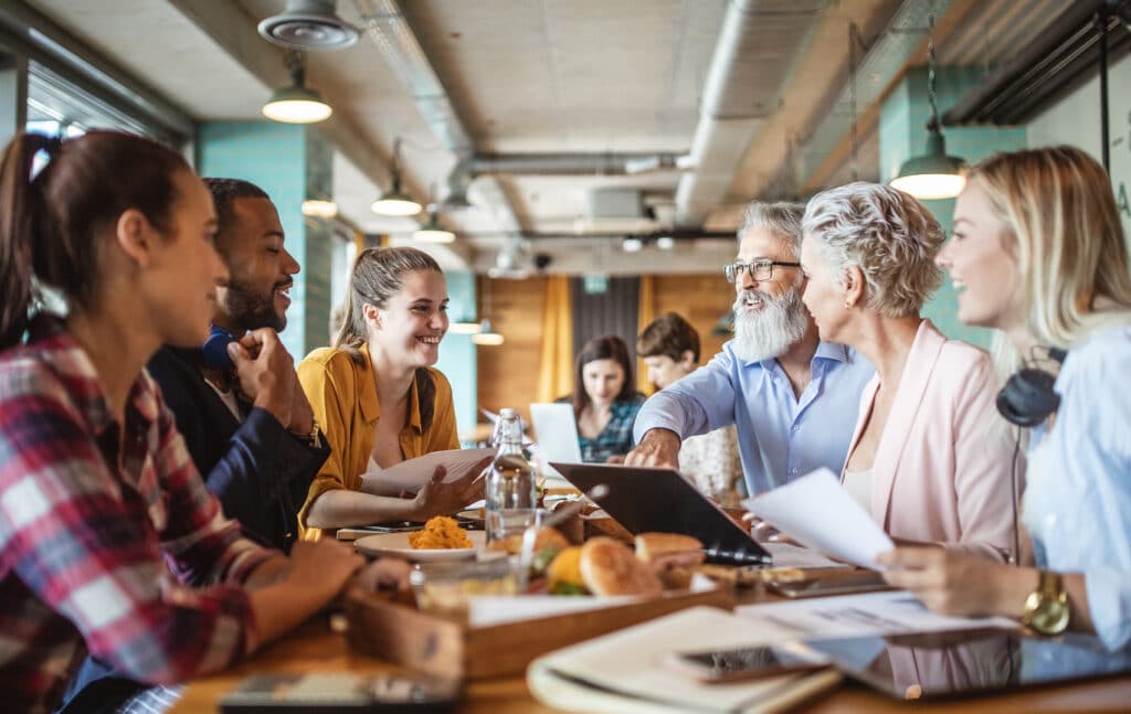 A group of smiling business people are having a language lunch in an office.