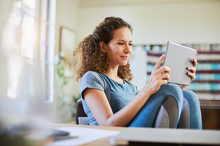 Lächelnde Frau lernt zu Hause auf ihrem Tablet.