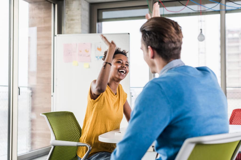 2 smiling co-workers are giving each other a high five.