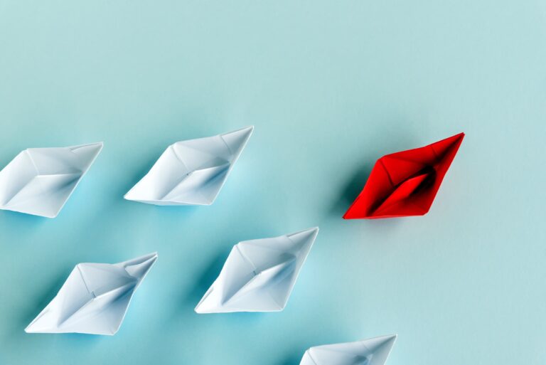Red paper ship leading white paper ships as a symbol of leadership.