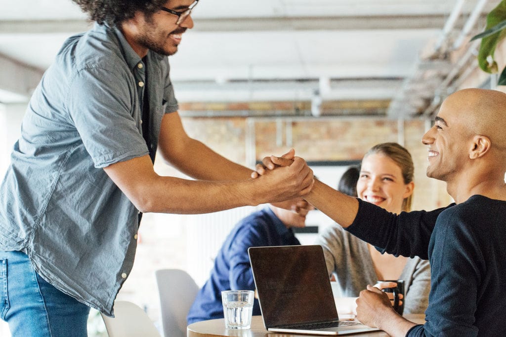 Smiling co-workers shake hands as a symbol of conflict resolution.