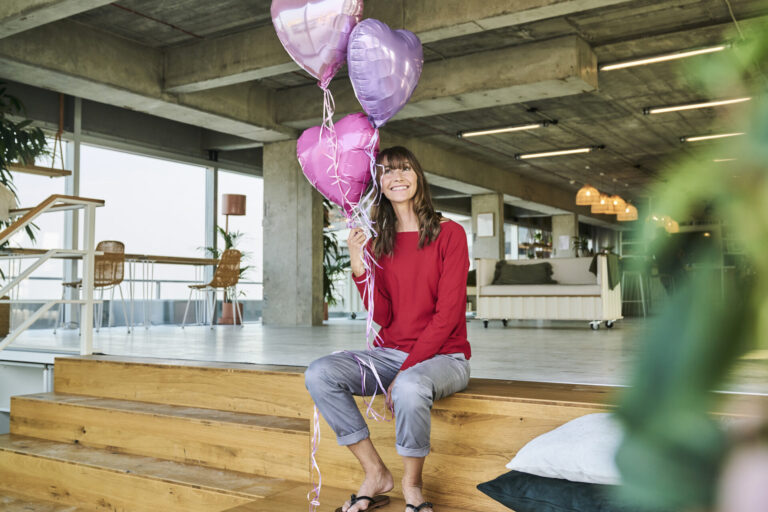 Happy employee holding heart-shaped balloons in an office.