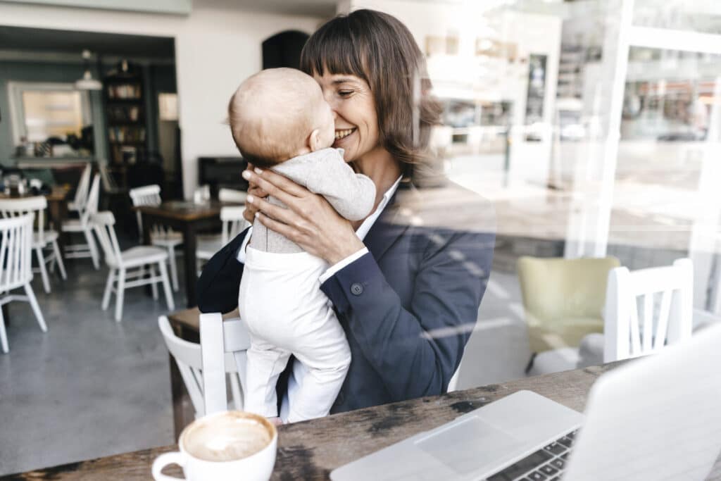 Smiling business woman sitting at the computer and holding up her baby.