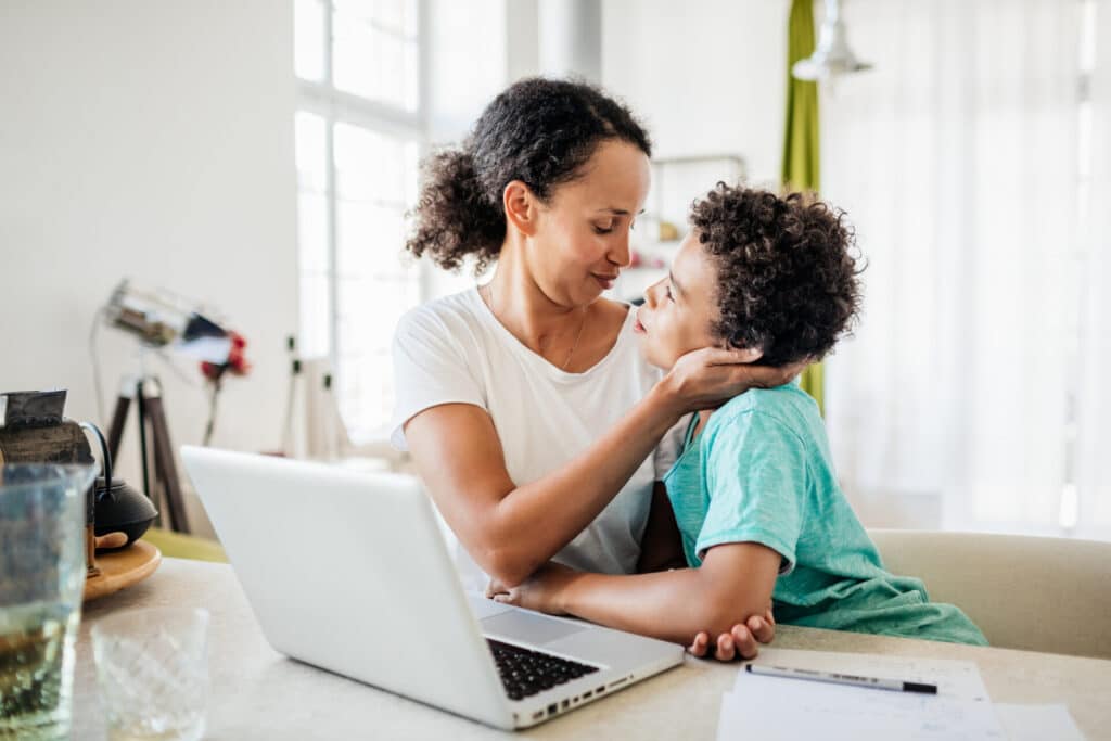 A mother sitting at the computer with her son and holding his face in her hands.