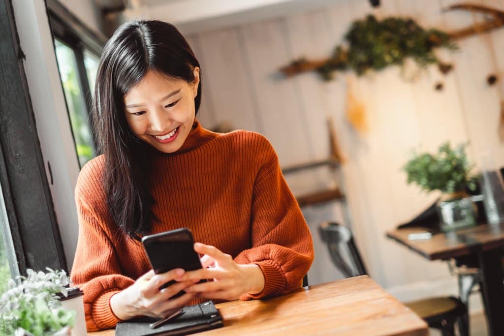 Lächelnde Geschäftsfrau aus der Finanzbranche lernt eine Sprache auf ihrem Smartphone.