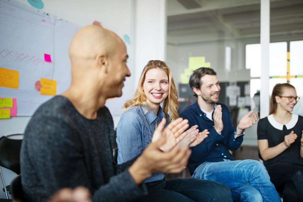 Lächelnde Mitarbeiter:innen klatschen nach einer Weiterbildung in die Hände.