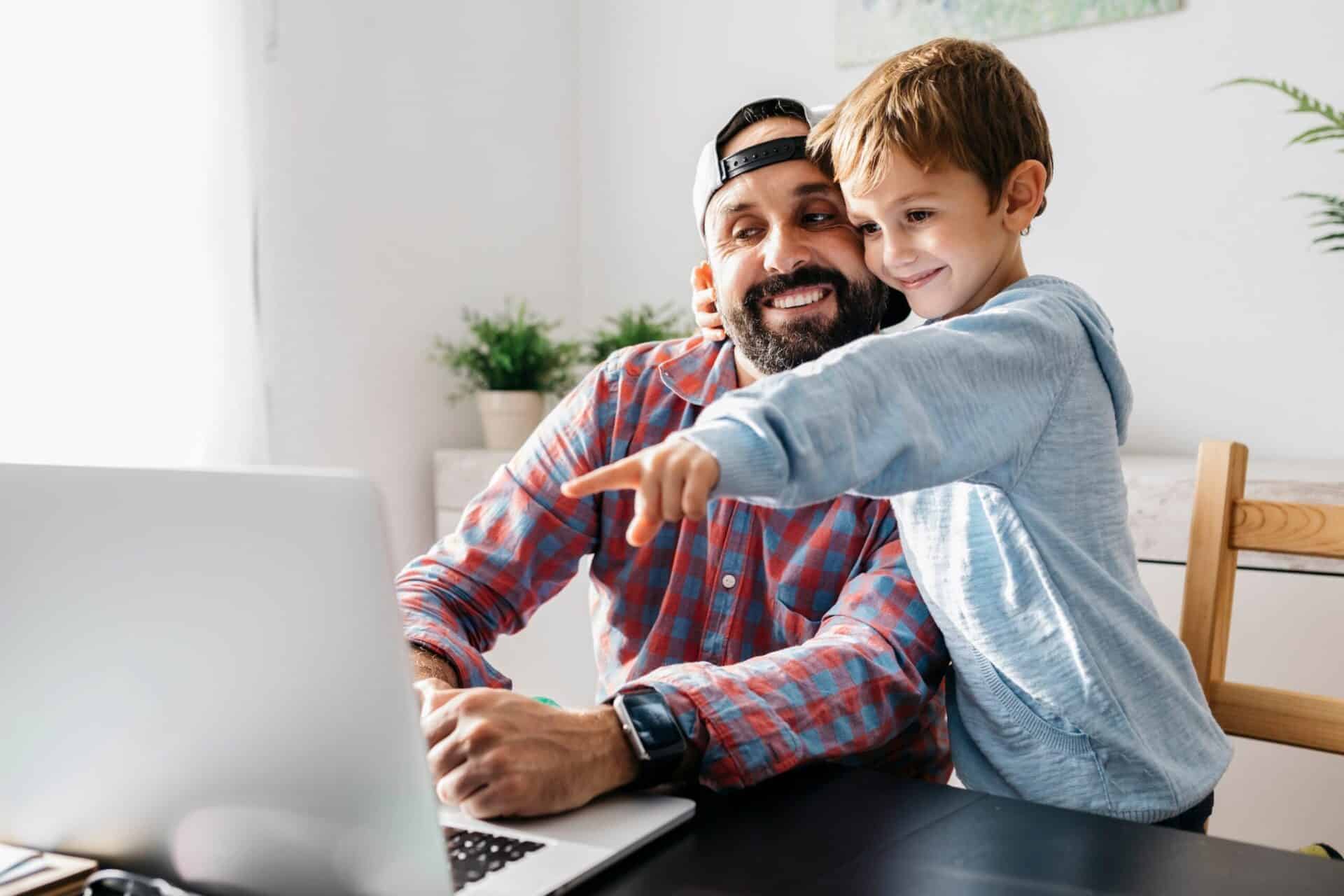 Lächelnder Vater und Sohn sehen sich etwas auf dem Laptop an.