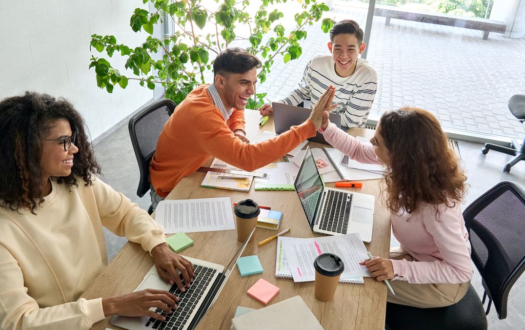 Ein fröhliches Team von Büroangestellten, die zusammen arbeiten und sich ein High Five geben.