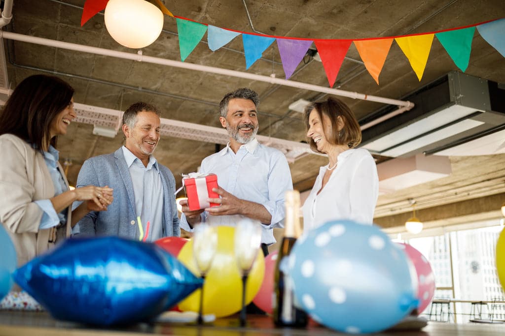 Fröhliche Mitarbeiter:innen feiern im Büro ein Jubiläum mit Konfetti und Geschenken.