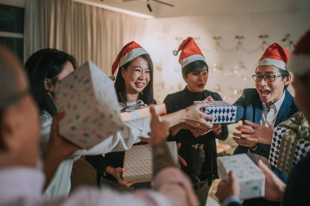 Feiernde Mitarbeiter:innen tauschen Weihnachtsgeschenke im Büro aus.