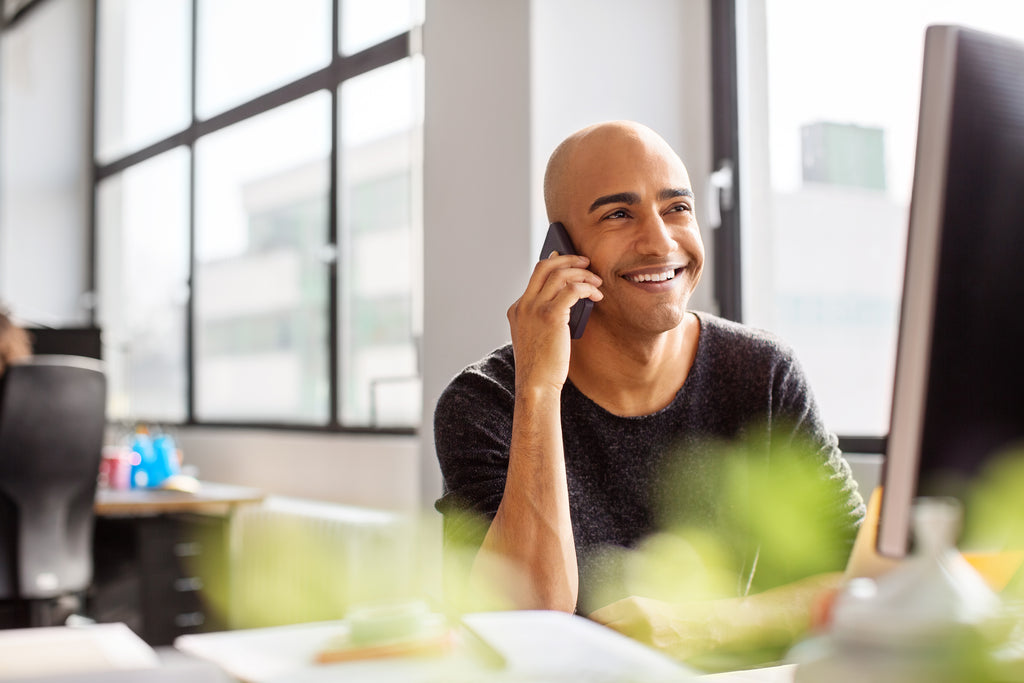 Lächelnder Büroangestellter kommuniziert über sein Smartphone mit einem Kundendienst.