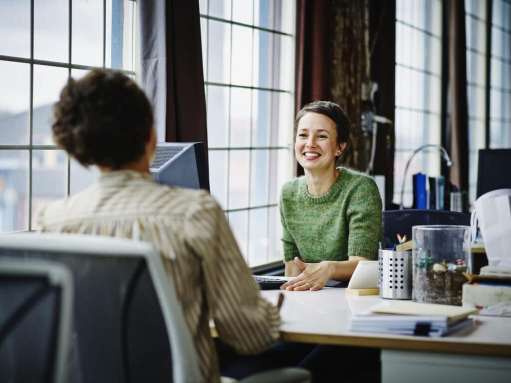 A smiling team lead is talking to a team member.