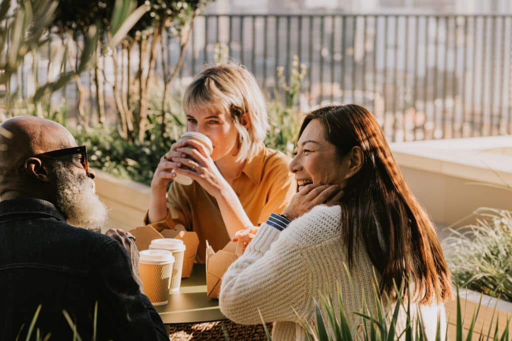 Smiling employees are sitting together at lunch and having a great employee experience.