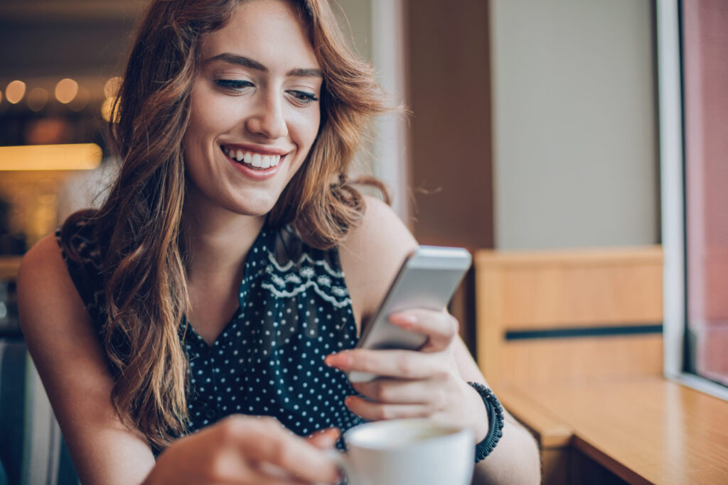 Smiling young woman holding her smartphone in a coffee shop, after having a great customer experience.