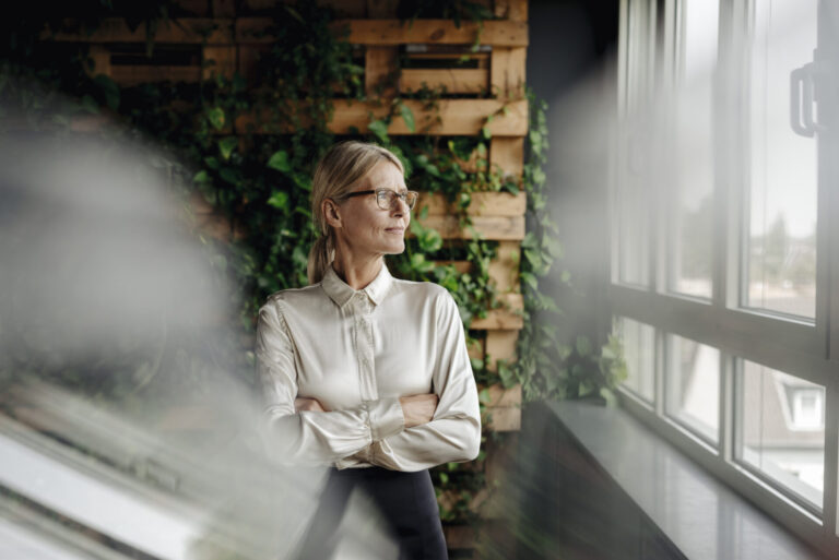 Geschäftsfrau steht in einem grünen Büro und sieht aus dem Fenster, als Symbol für die Zukunft.