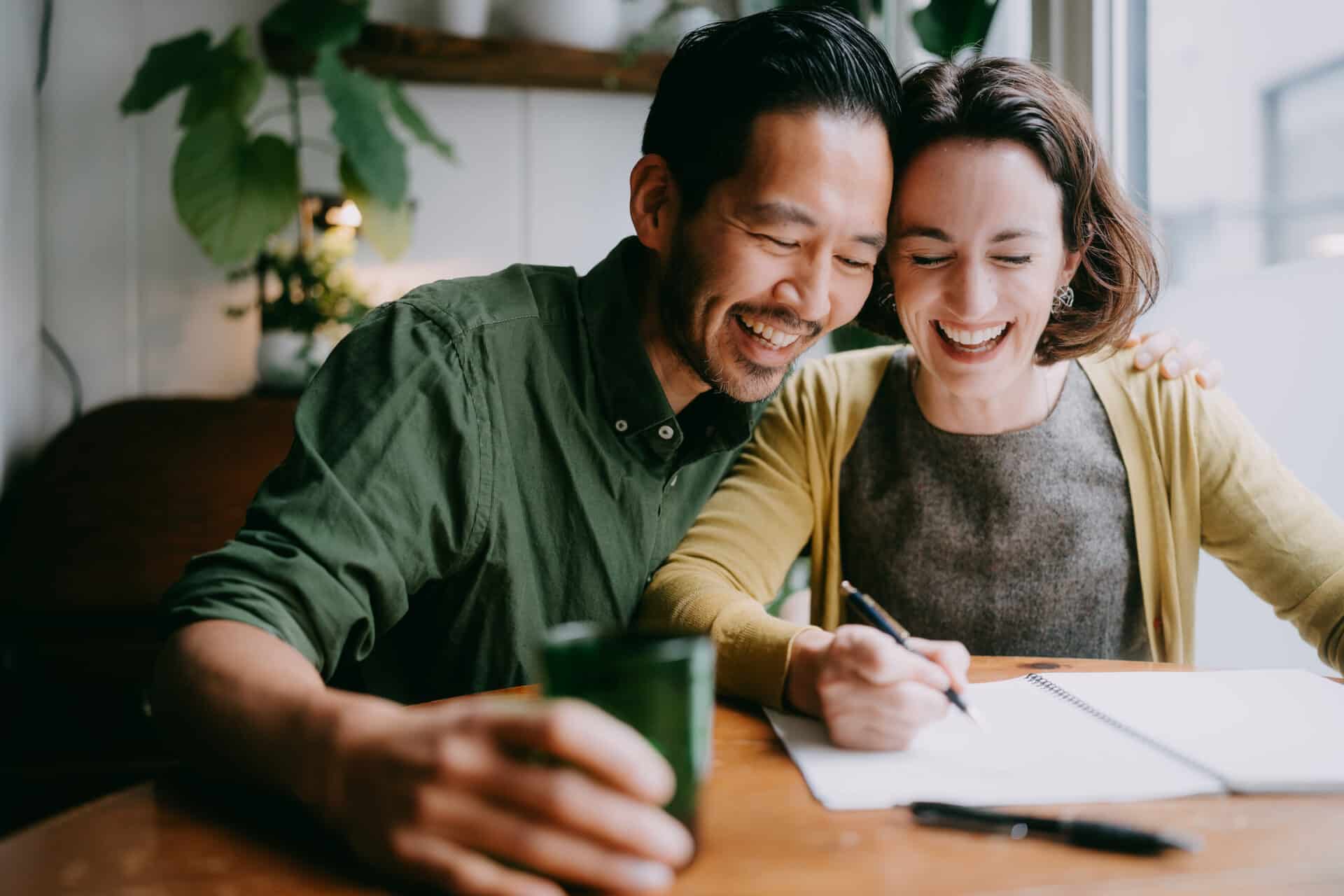 Two smiling people are learning a language together in their home.