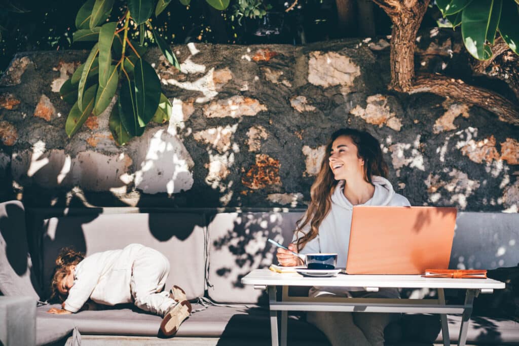 Eine junge Mutter sitzt mit ihrem Kleinkind in einem Café und arbeitet an ihrem Laptop, da sie flexible Arbeitsregelungen hat.