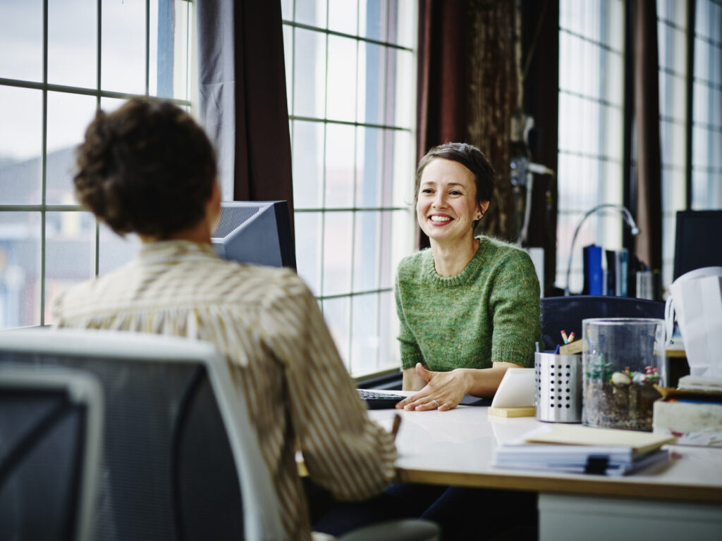 Two smiling business women are talking in an office, as a symbol of recruiting.