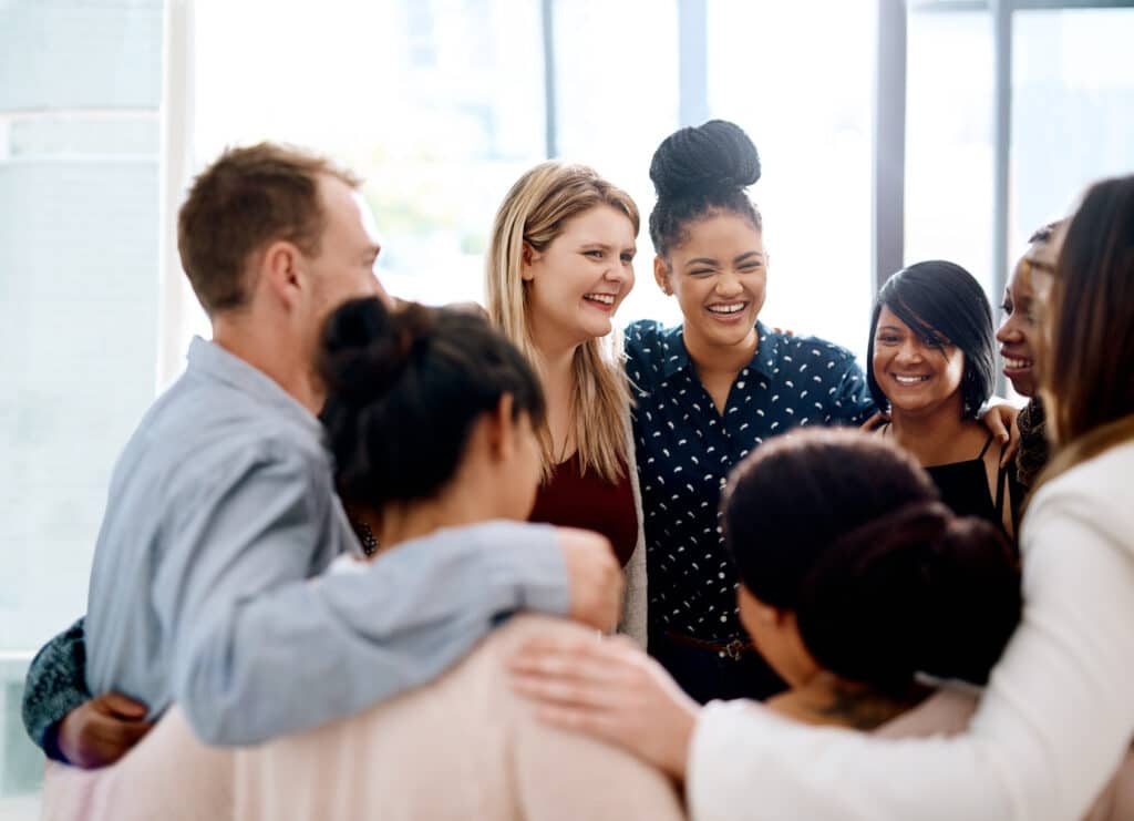 Smiling young business people are standing arm in arm in the office, as a symbol of being appreciated at work.